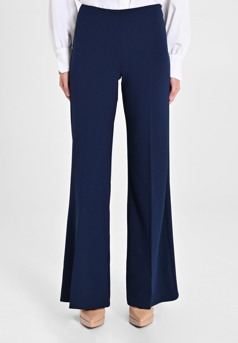 Pantalons larges bleu marine en tissu lisse et extensible, avec une taille haute et une silhouette fluide, associés à des talons beiges.