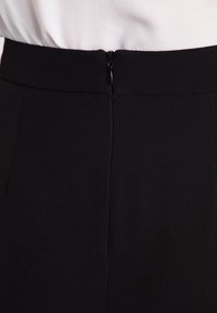 Svart tygkjol med en dold dragkedja baktill och en slät, texturerad yta. Enkel, skräddarsydd design utan mönster.