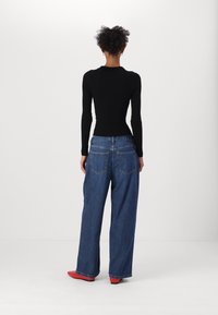 Černý žebrovaný top s dlouhým rukávem, modré široké džíny s vysokým pasem, červené boty, zadní pohled, minimální detaily s viditelnými švy a zadními kapsami.