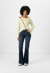 Yellow ribbed sweater with a diagonal button-down opening, paired with dark blue flared jeans and white ankle boots.