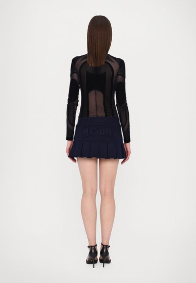 Sort mesh langærmet top med vertikalt stribemønster, parret med en marineblå plisseret mini-skirt med det prægede brandnavn "MISBHV."