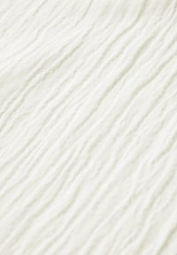 Tejido texturizado en color blanco roto, que presenta líneas suaves y onduladas en la superficie, transmitiendo una apariencia táctil y delicada.