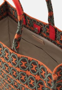Sac fourre-tout en tissu tissé avec un motif orange, vert et noir, poignées en cuir rouge et intérieur beige avec une poche.