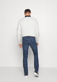Hallus hall sweatshirt, mis on ühendatud tumesiniste slim-fit teksadega. Teksadel on tagakotid ja kerged õmblusestiku üksikasjad.