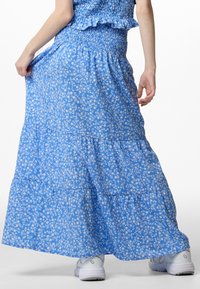 Blue floral maxi skirt with a smocked waist, featuring layered tiers and a lightweight fabric. White floral pattern throughout.