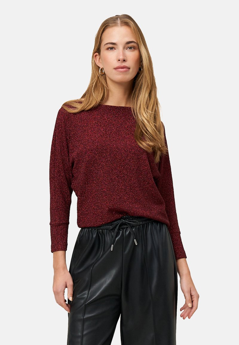 Haut rouge scintillant à manches longues avec un large décolleté, associé à un pantalon en cuir noir doté d'une taille à cordon et d'une coupe décontractée.