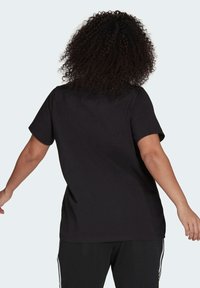 Černé bavlněné tričko, krátké rukávy, volný střih, kulatý výstřih, minimalistický design, osoba otočená zády, v kombinaci s černými kalhotami.