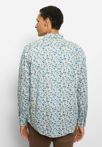 Langärmeliges Hemd aus hellblauem Stoff mit floralem Muster in Blau-, Braun- und Orangetönen, mit Knopfmanschetten und abgerundetem Saum.