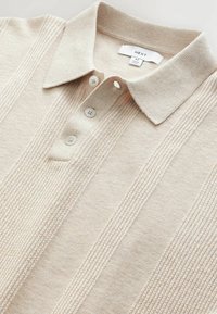 Polo shirt beige clair en tissu doux, doté de trois boutons, d'un col et de détails en tricot vertical le long de l'avant.