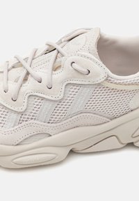 Sapatilhas em malha cinza claro com detalhes em camurça, sola espessa em creme, superfície texturizada e um design ondulado único na parte superior.