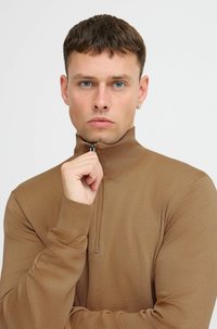 Karcsú szabású, cipzáros kardigán meleg barna árnyalatban, texturált kötött anyagból készült. Magas gallérral és bordázott mandzsett�ákkal rendelkezik.