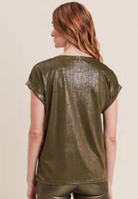 Olijfgroene t-shirt met een glanzend, gestructureerd oppervlak, korte mouwen en een relaxte pasvorm, met een ronde hals en opgerolde mouwmanchetten.