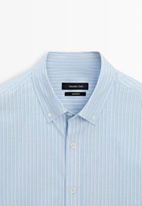 Camicia azzurra a righe con linee verticali sottili, colletto classico e bottoni bianchi. Le etichette riportano "Massimo Dutti" e "Made in Egypt."