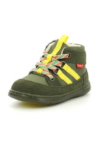 Zapato infantil de tela verde y ante con cordones amarillos y multicolores, que presenta tres rayas amarillas, suela de goma texturizada y detalle de logotipo.
