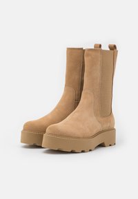 Tan suede ankle boots with elastic side panels, round toe, thick platform sole with textured tread, and pull tabs on the heel for easy wear.