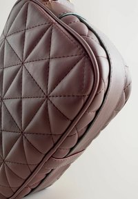Quilted bordeaux leren tas met een geometrisch patroon, zilveren hardware en een zijrits. Zachte textuur met een strak design.