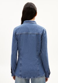 Dunkelblaue Jeansjacke mit einem kragenlosen Ausschnitt, langen Ärmeln und Knopfmanschetten; zeichnet sich durch eine taillierte Silhouette und einen strukturierten Stoff aus.