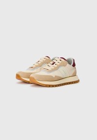 Un paio di sneakers casual beige e tan con lacci bianchi, dettagli color bordeaux sul tallone e suole in gomma testurizzata su uno sfondo bianco semplice.
