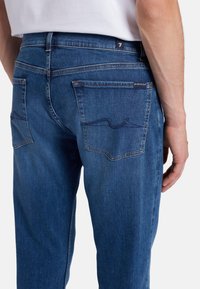 Jeans in denim blu con una vestibilità regolare, dotati di due tasche posteriori, dettagli di cucitura discreti e una vita a media altezza.