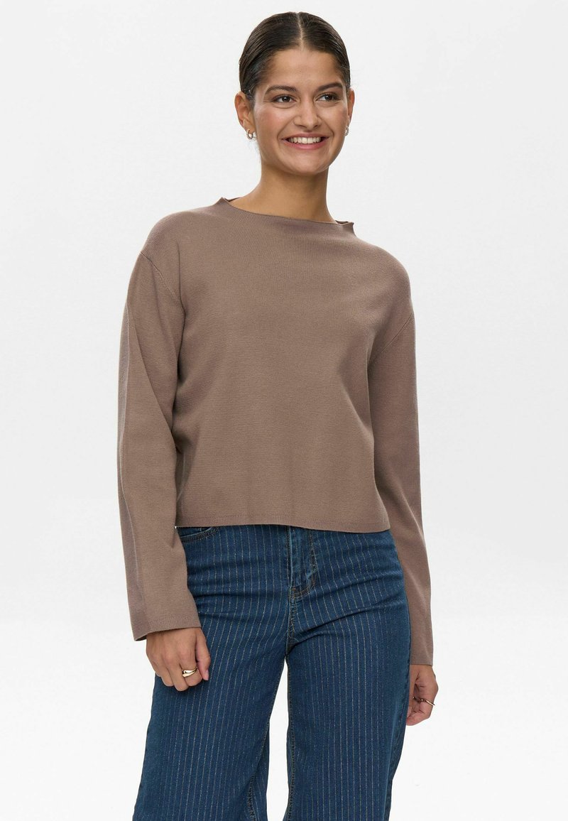 Maglione marrone a maniche lunghe con texture a coste e un design leggermente accorciato. Abbinato a jeans blu a righe verticali a vita alta.