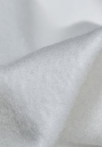 Gros plan d'un matériau doux, blanc, fibreux avec une surface texturée, duveteuse et des plis doux.