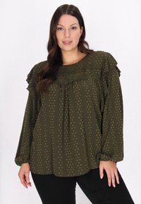 Mørkegrøn bluse med ruffled skuldre, prikket mønster i en lysere nuance og en struktureret yoke. Lange ærmer med elastiske manchetter.