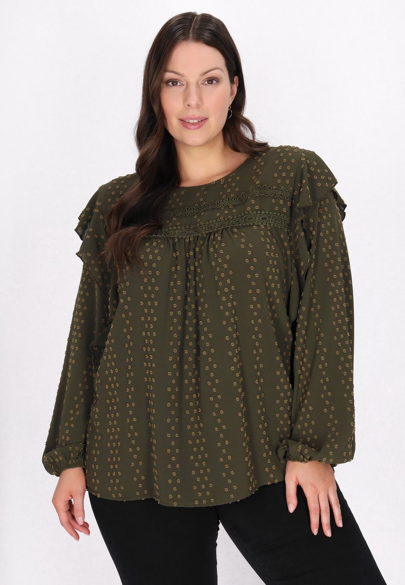 Mørkegrøn bluse med ruffled skuldre, prikket mønster i en lysere nuance og en struktureret yoke. Lange ærmer med elastiske manchetter.
