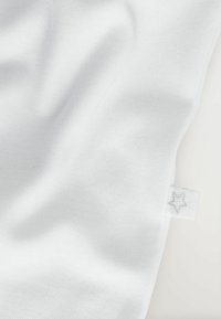 Witte stof met een zachte, gestructureerde weving en een zichtbaar genaaide label met een sterlogo. Gladde en uniforme oppervlakte.