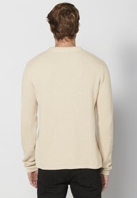 Beige geribbelde lange mouw trui met een ronde hals, aangesloten mouwen en een licht verlengde achterzoom. Eenvoudige en gestructureerde stof.