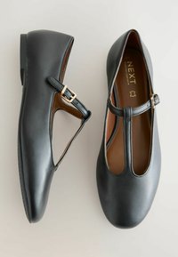 Pár černých kožených balerín s T-řemínkem Mary Jane, zlatou sponou a zaoblenou špičkou, zobrazený z horního a bočního pohledu na neutrálním pozadí.