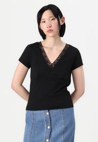 Svart T-skjorte med dyp V-hals og blonder, kortermet og tettsittende design, kombinert med et denimskjørt.