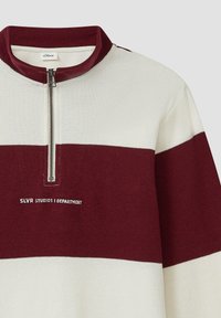 Halb-Zip-Pullover in Kastanienbraun und Creme mit gerippter Textur, hoher Kragen und gesticktem Logo, kombiniert mit horizontalen Farbblöcken.