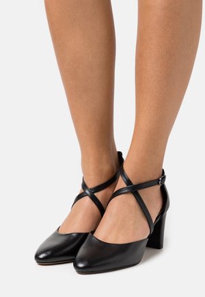 Musta nahkakengät korkokengät teräväkärkiset, nilkkaketjuilla ristiin etuosassa ja tukevat paksut korot. Sileä pinta kauttaaltaan.