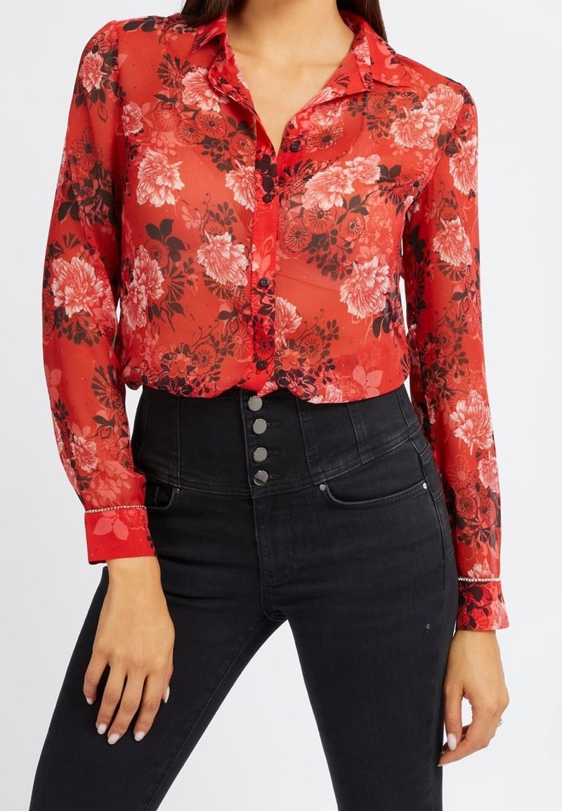 Blusa de botones roja con estampado floral, de textura semitransparente, que presenta patrones florales negros y un cuello con solapa. Combinada con pantalones negros de cintura alta.