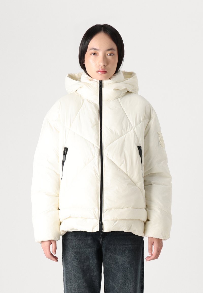 Balta pūka jaka ar kapuci, ar dimanta stīvējuma rakstu, priekšējo rāvējslēdzēju un sānu kabatām ar melniem aksesuāriem.