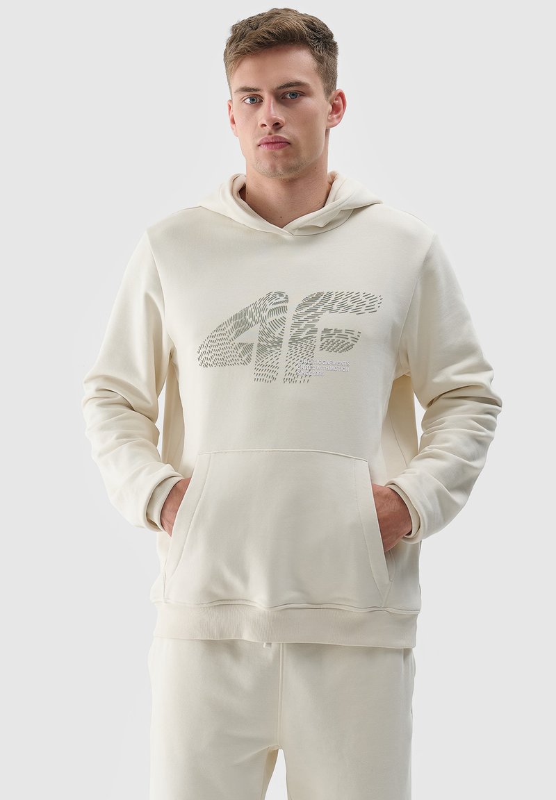 Crème-kleurige hoodie van zacht materiaal, met een voorzak in kangoeroestijl en een grafisch logo ontwerp op de borst.