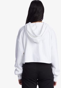 Weißer, verkürzter Hoodie mit Kapuze, langen Ärmeln und gerippten Bündchen. Kombiniert mit schwarzen Hosen, die ein einfaches und funktionales Design präsentieren.