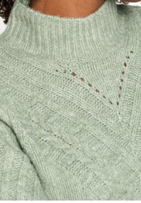 Pull en tricot vert clair avec un col montant, présentant un motif texturé et de subtils accents diagonaux. Matériau doux et confortable.