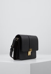 Borsa a tracolla nera in pelle con un design strutturato, chiusura in metallo dorato e tracolla regolabile. Texture liscia con una finitura leggermente grana.