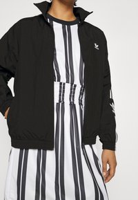 Svart vindjacka med dragkedja fram och elastiska ärmar. I kombination med en randig klänning i vitt och svart med rynkad midja.