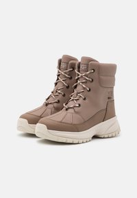 Brązowe skórzane buty za kostkę, z okrągłym noskiem, wyściełanym kołnierzem i fakturowaną powierzchnią. Posiadają beżowe sznurowadła oraz masywną białą podeszwę.