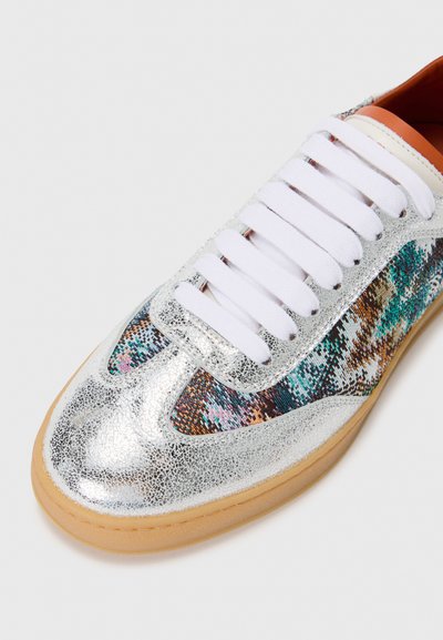 Silver metallic sneakers with white laces, featuring multicolored textile accents and a light brown rubber sole. Textured surface detail visible.