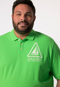 Zielona koszulka polo z kołnierzykiem, trzema guzikami i białym logo żaglówki z napisem "SAILOR 53.281534." Gładka tekstura i żywy kolor.