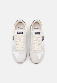 Scarpe sportive bianche con texture in suede e mesh, dotate di lacci color crema. Comprendono una patch loghi blu navy e accenti a strisce sui lati.