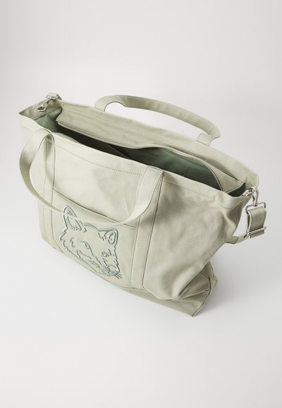 Bolso tote de lona verde claro con cierre superior, que presenta un diseño grabado de un zorro en la parte frontal y asas resistentes para el hombro. El interior también es verde.
