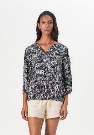 Navy blouse with white speckled pattern, V-neck, and three-quarter sleeves. Paired with beige shorts, minimalistic design and loose fit.