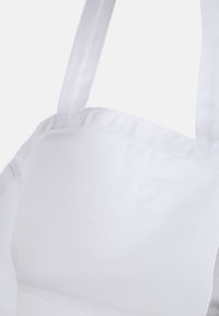 Sac fourre-tout en coton blanc avec un tissu robuste, des anses larges et un intérieur propre et lisse. Design minimal, sans motifs ni accents supplémentaires.