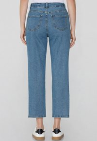 Jeans de mezclilla azul de cintura alta con corte recto, dos bolsillos traseros y costuras visibles, combinados con zapatillas blancas con detalles negros.