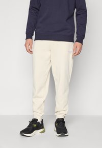 Sweatshirt bleu marine, associé à un pantalon de jogging crème. Tenue complétée par des chaussures de sport noires avec des accents verts et un design épuré.