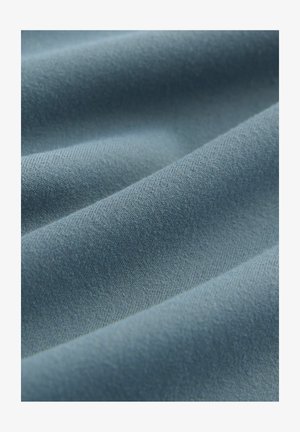 Pehme, tekstuuriga kangas tuhmides sinistes toonides, millel on sile pind ja diagonaalne kootud muster, mis näitab peent sügavust ja rikkust.